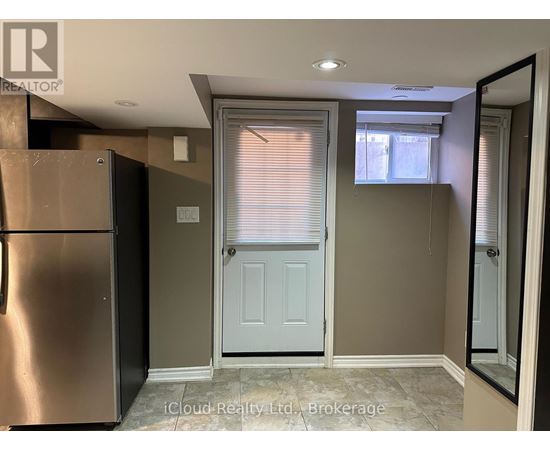 A kitchen with a refrigerator, a door, and a window with blinds.