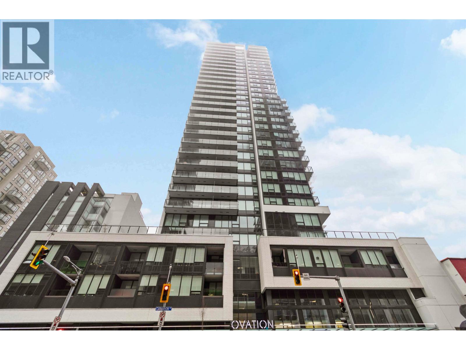 A tall building with a glass facade stands in front of other buildings.