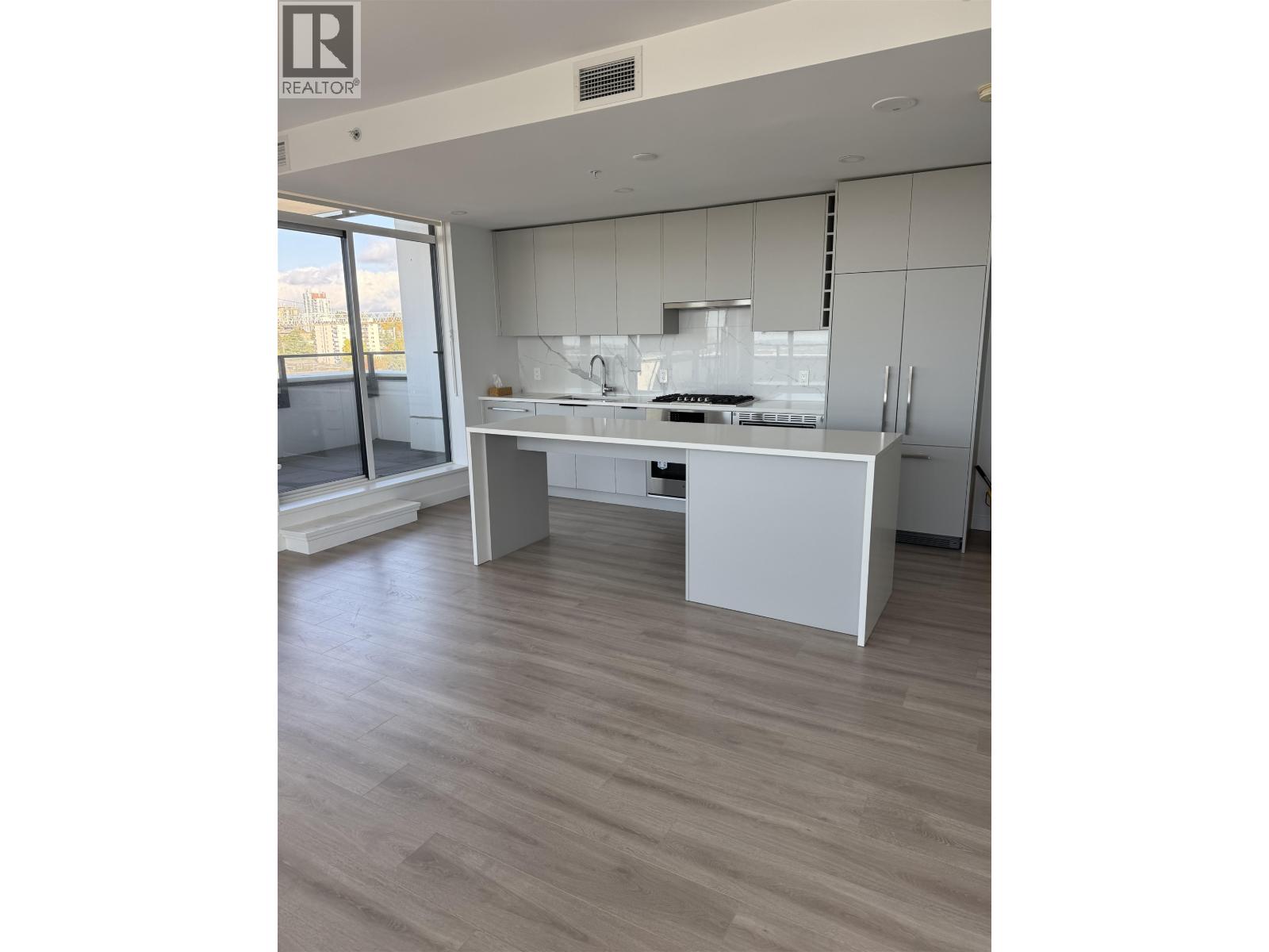 A modern kitchen with white cabinets and a wooden floor.