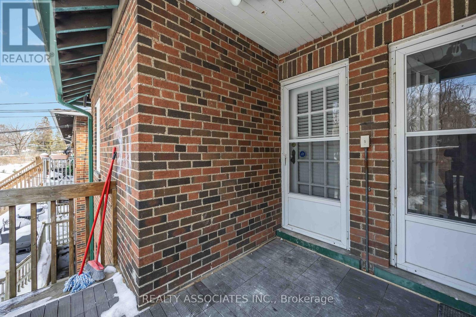 A red broom stands on a porch with a white door.