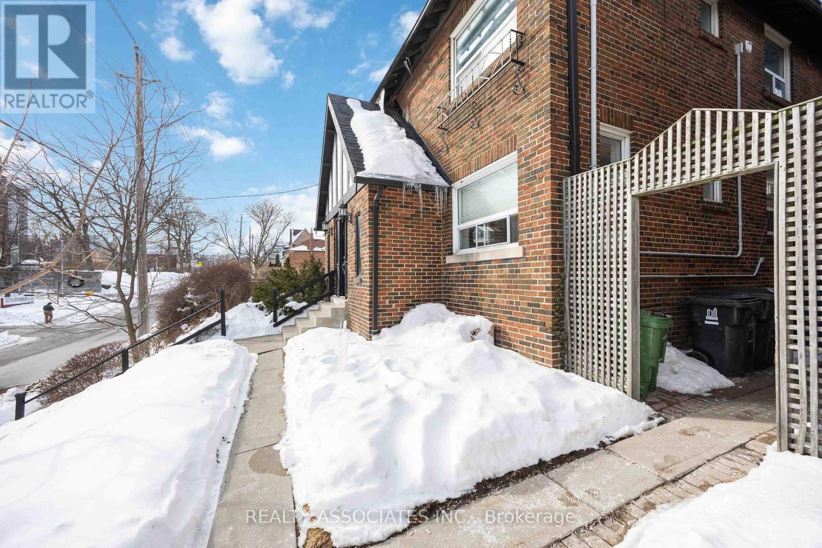 A snow-covered sidewalk leads to a brick building with a balcony.