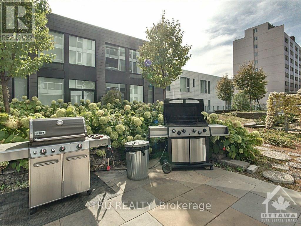 A BBQ grill is in the middle of a patio surrounded by trees and bushes.
