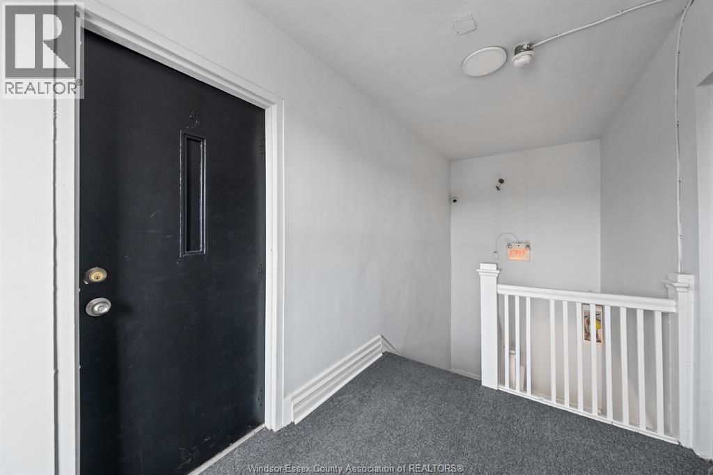 A black door with a gold handle is on the left of a room with a white ceiling and a white crib.