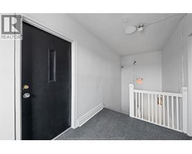 A black door with a gold handle is on the left of a room with a white ceiling and a white crib.