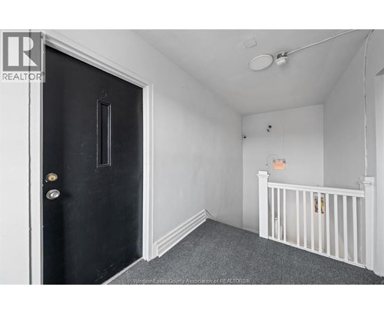 A black door with a gold handle is on the left of a room with a white ceiling and a white crib.