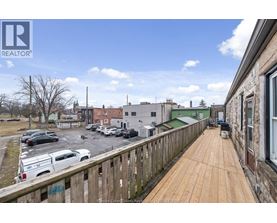 A balcony with a wooden floor overlooks a parking lot and buildings.