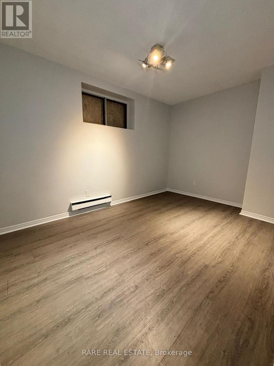 A room with wood flooring and a window with a white wall.