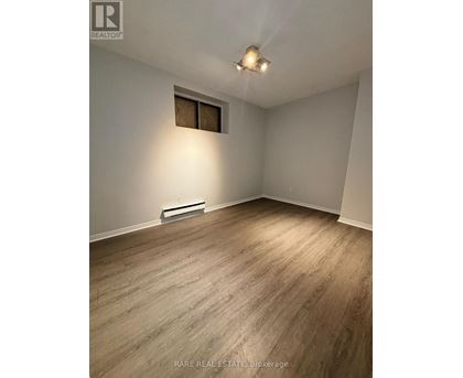 A room with wood flooring and a window with a white wall.