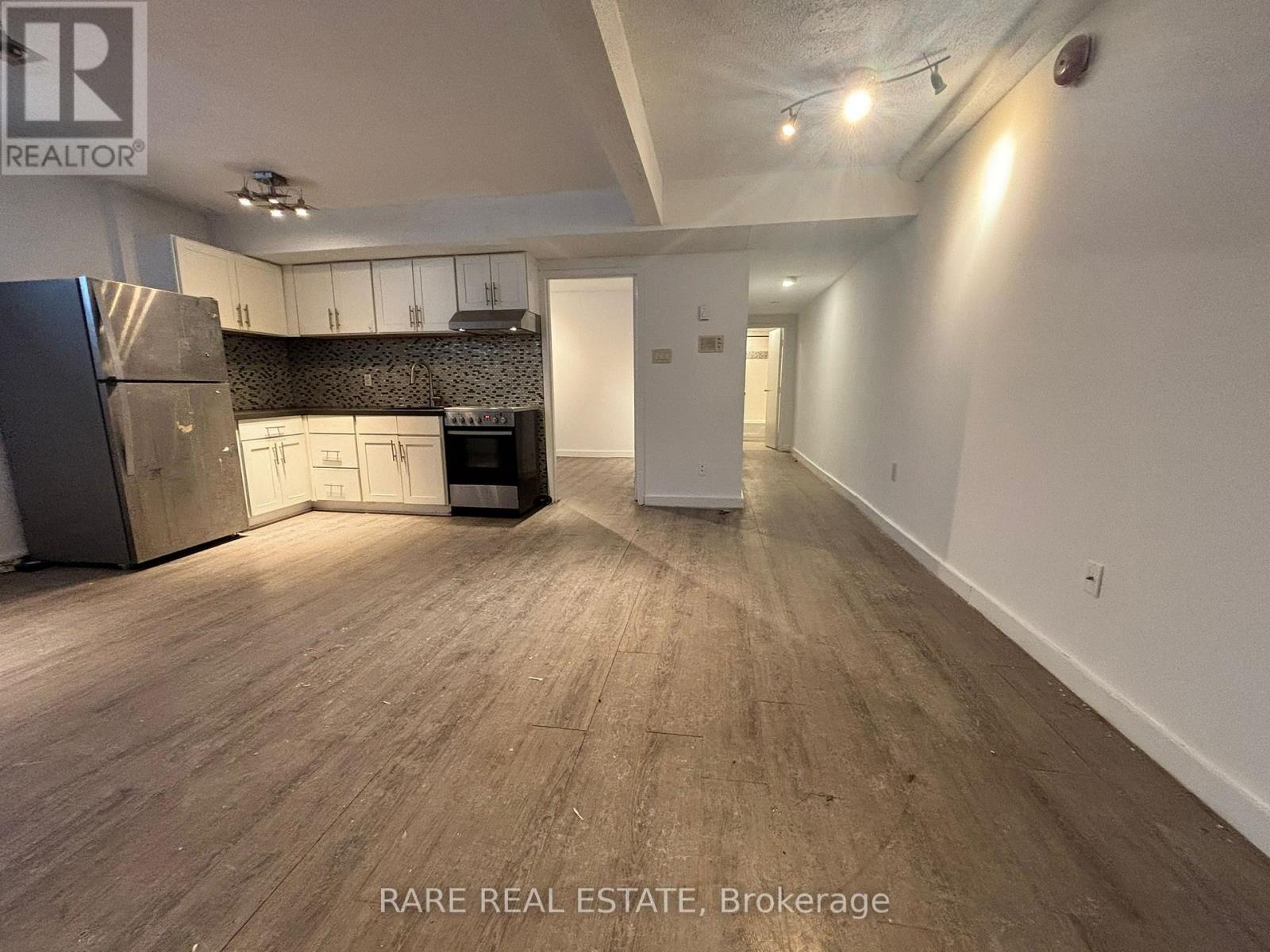 A spacious room with wooden flooring and a kitchen area with white cabinets and appliances.