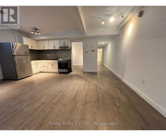 A spacious room with wooden flooring and a kitchen area with white cabinets and appliances.