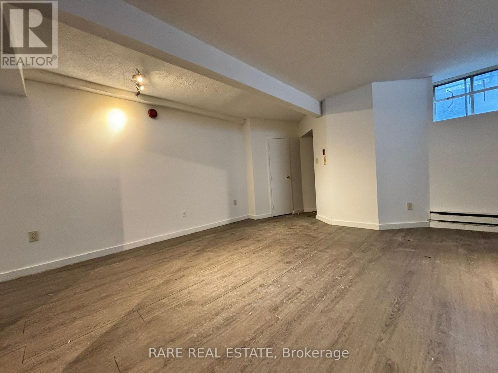 A room with wooden flooring and white walls, with a window on the right side.