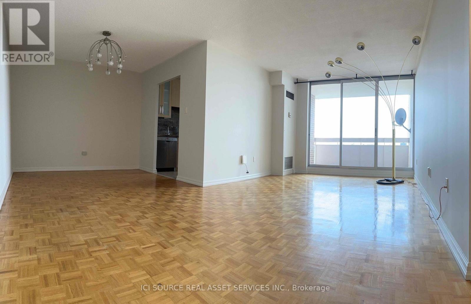 A large empty room with wooden flooring and a chandelier.