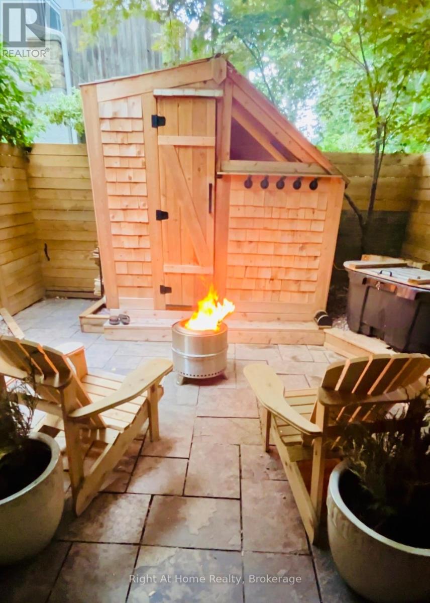 A wooden hot tub is surrounded by wooden chairs in a backyard.
