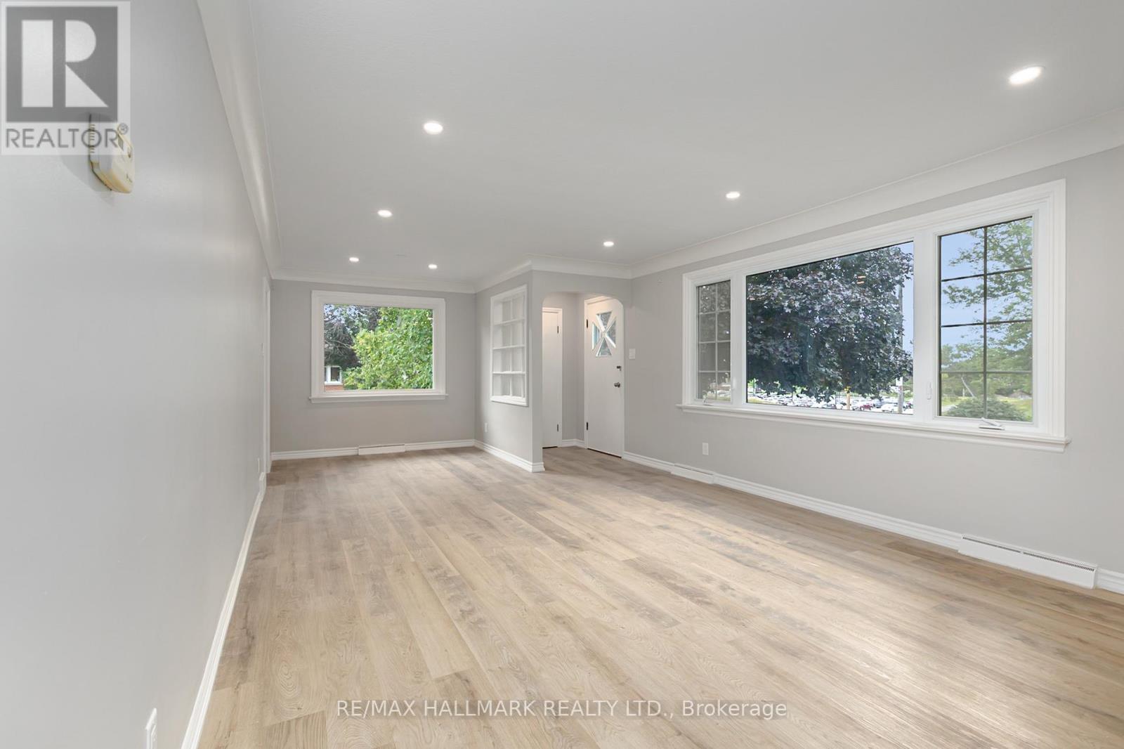 A spacious room with wooden flooring and white walls, with windows on one side.