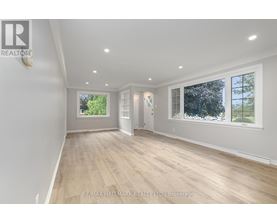 A spacious room with wooden flooring and white walls, with windows on one side.