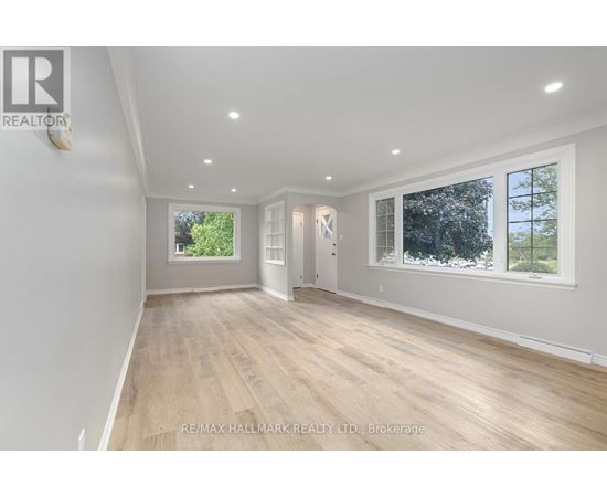 A spacious room with wooden flooring and white walls, with windows on one side.