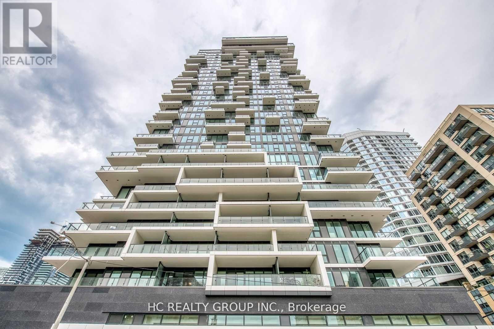 A tall residential building with balconies and a sign for HC Realty Group Inc. in Brokerage.