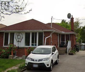 A white car is parked in front of a brick house.