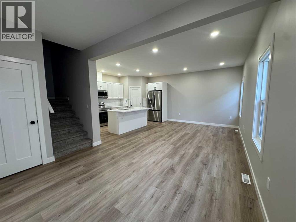 A spacious room with wooden flooring and a kitchen area in the background.