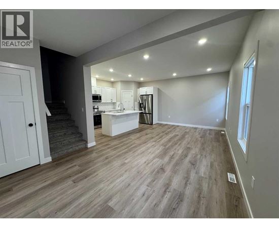 A spacious room with wooden flooring and a kitchen area in the background.