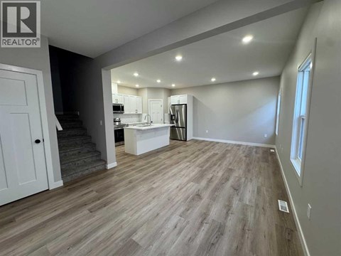 A spacious room with wooden flooring and a kitchen area in the background.