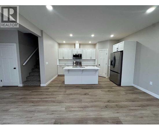 A well-lit kitchen with a refrigerator, sink, and cabinets.