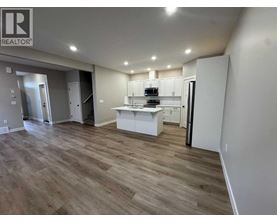 A well-lit, spacious kitchen area with wooden flooring and white cabinetry.