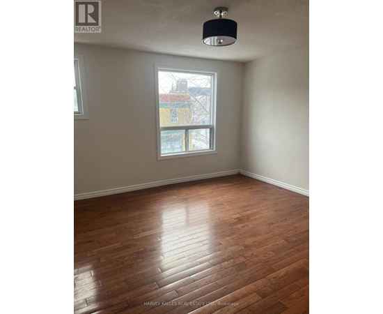 A room with wooden flooring and a window showing a view of a building outside.