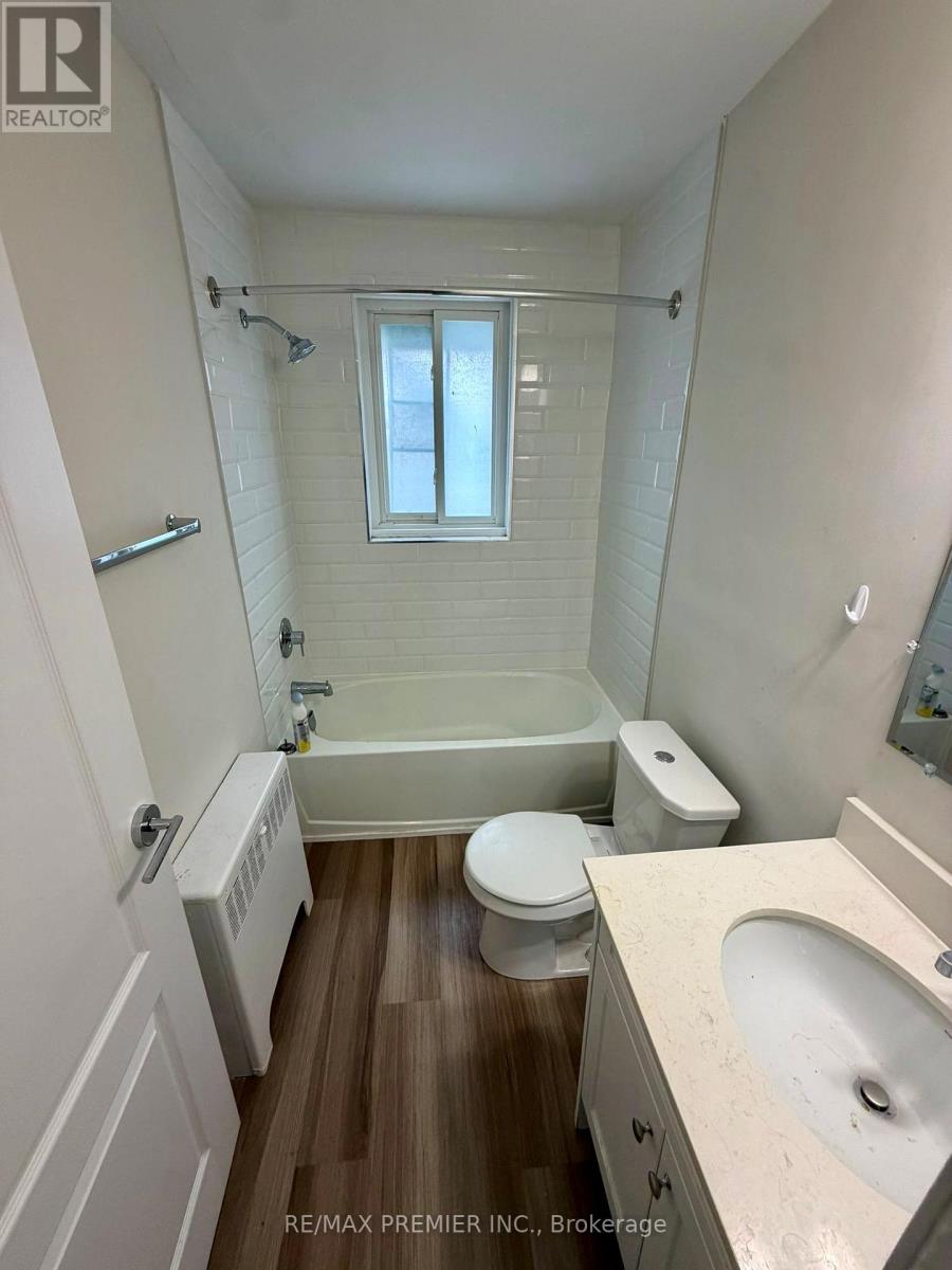 A white bathroom with wood flooring and a window.