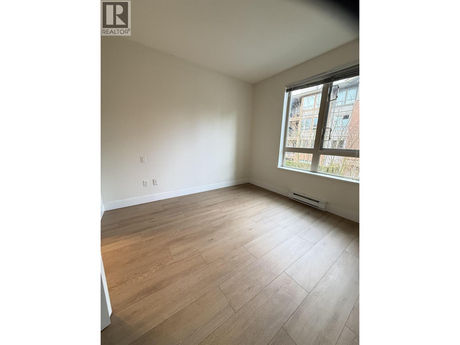 A room with wooden flooring and a window overlooking a building.