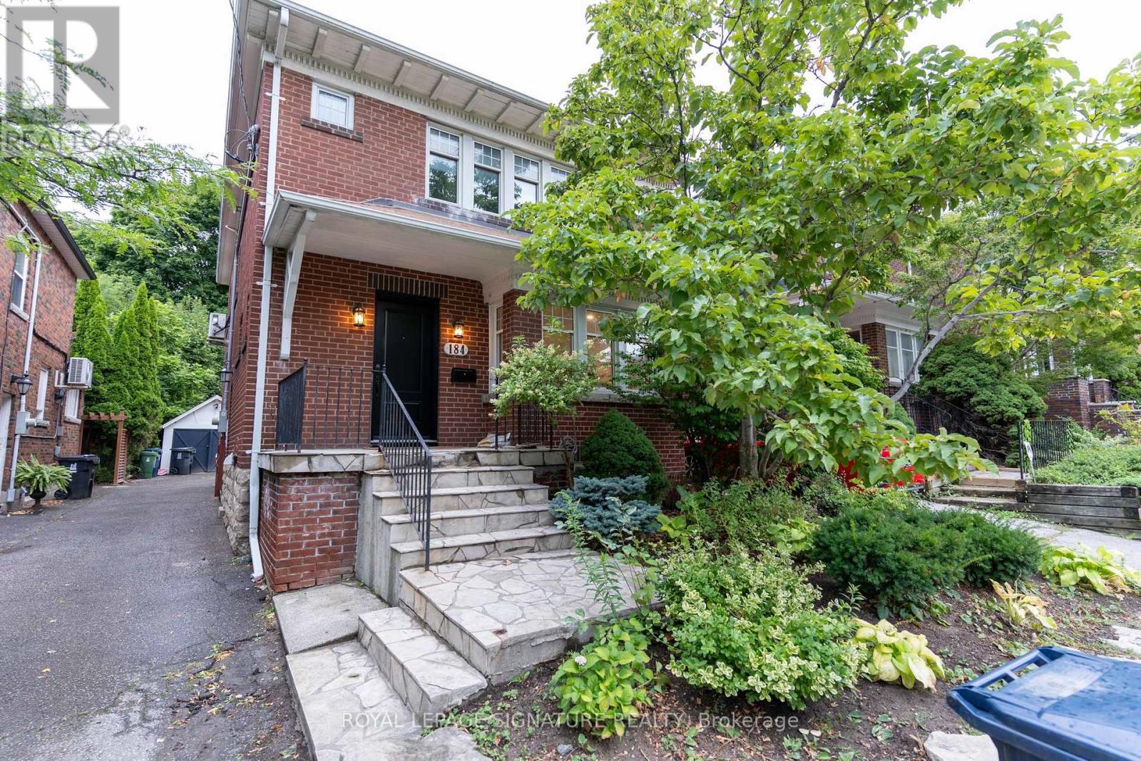 A house with a red brick facade and a black door is surrounded by greenery.