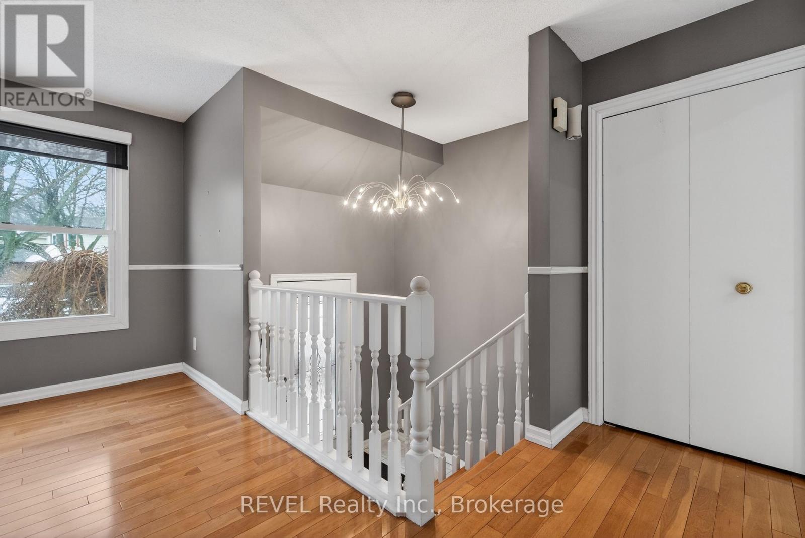 A white staircase with a chandelier in a room with wooden floors.