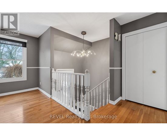 A white staircase with a chandelier in a room with wooden floors.