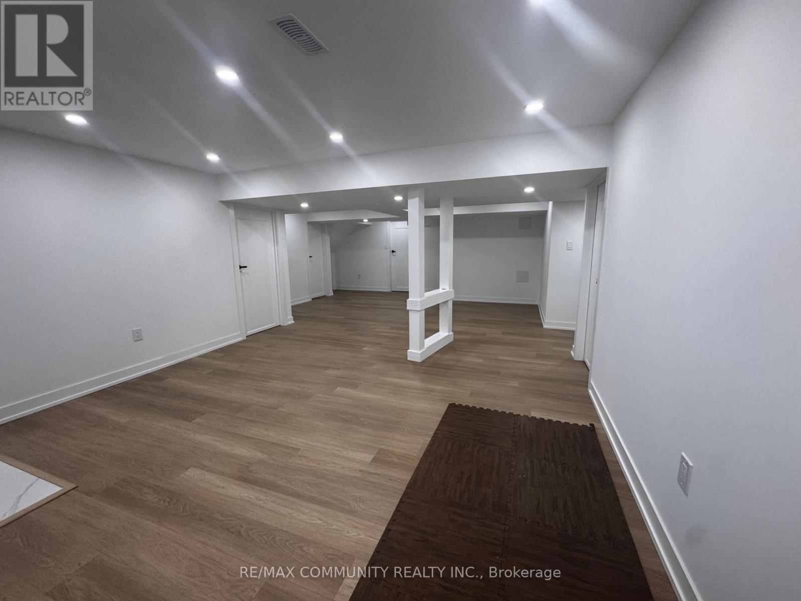 A spacious room with wooden flooring and white walls, with a brown rug on the floor.