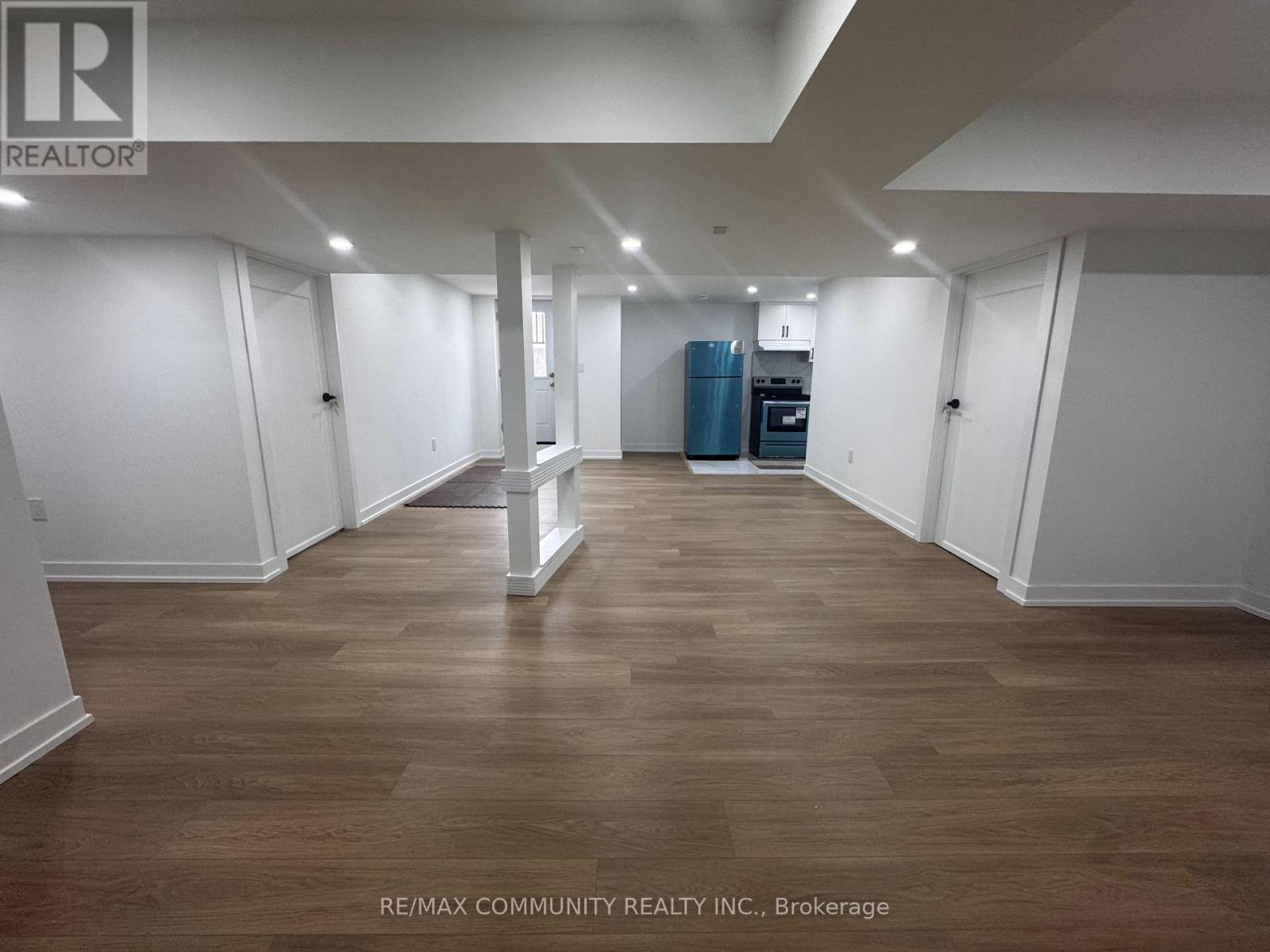 A spacious room with wooden flooring and white walls, furnished with a kitchenette.