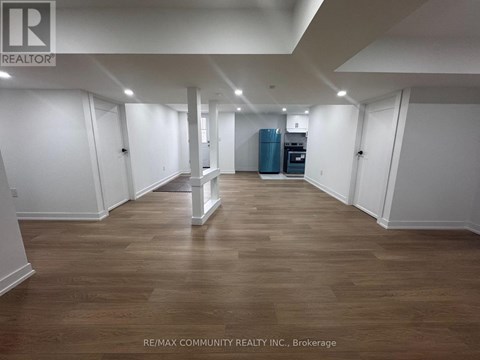 A spacious room with wooden flooring and white walls, furnished with a kitchenette.