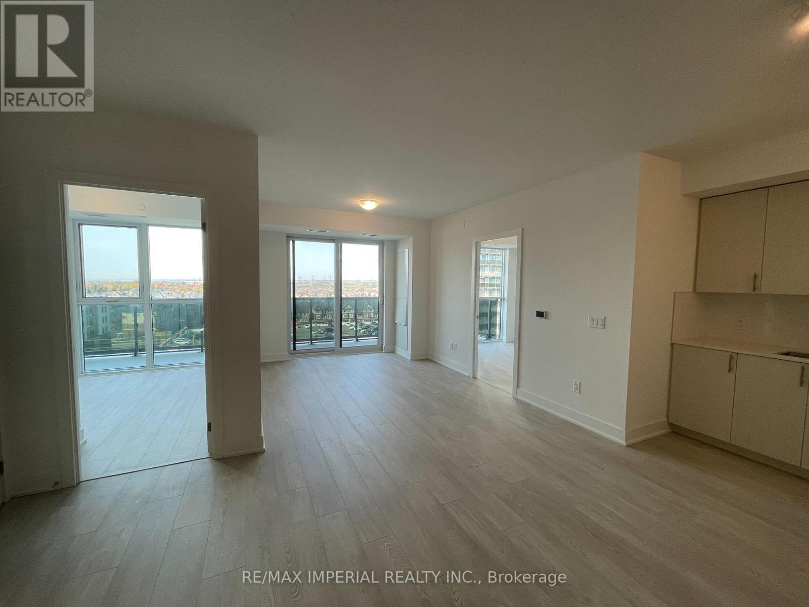 A spacious room with wooden flooring and large windows overlooking a cityscape.