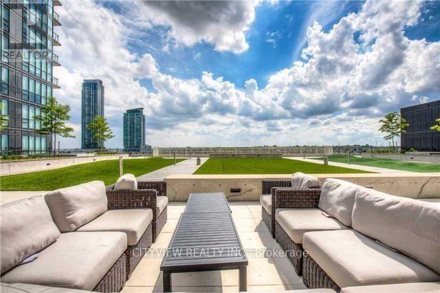 A patio with a table and chairs overlooking a grassy area and buildings.