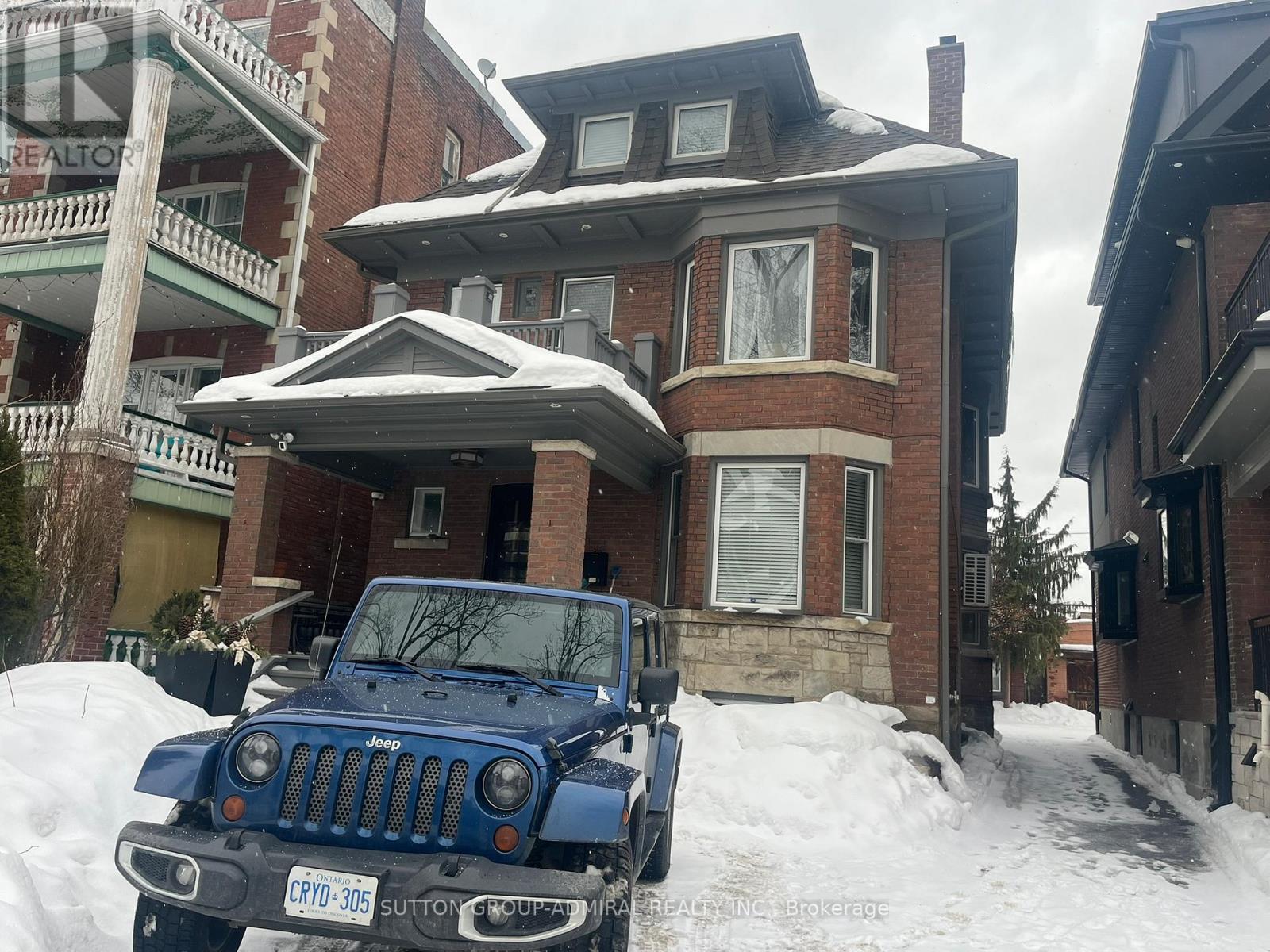 A blue Jeep is parked in front of a house with snow on the ground.