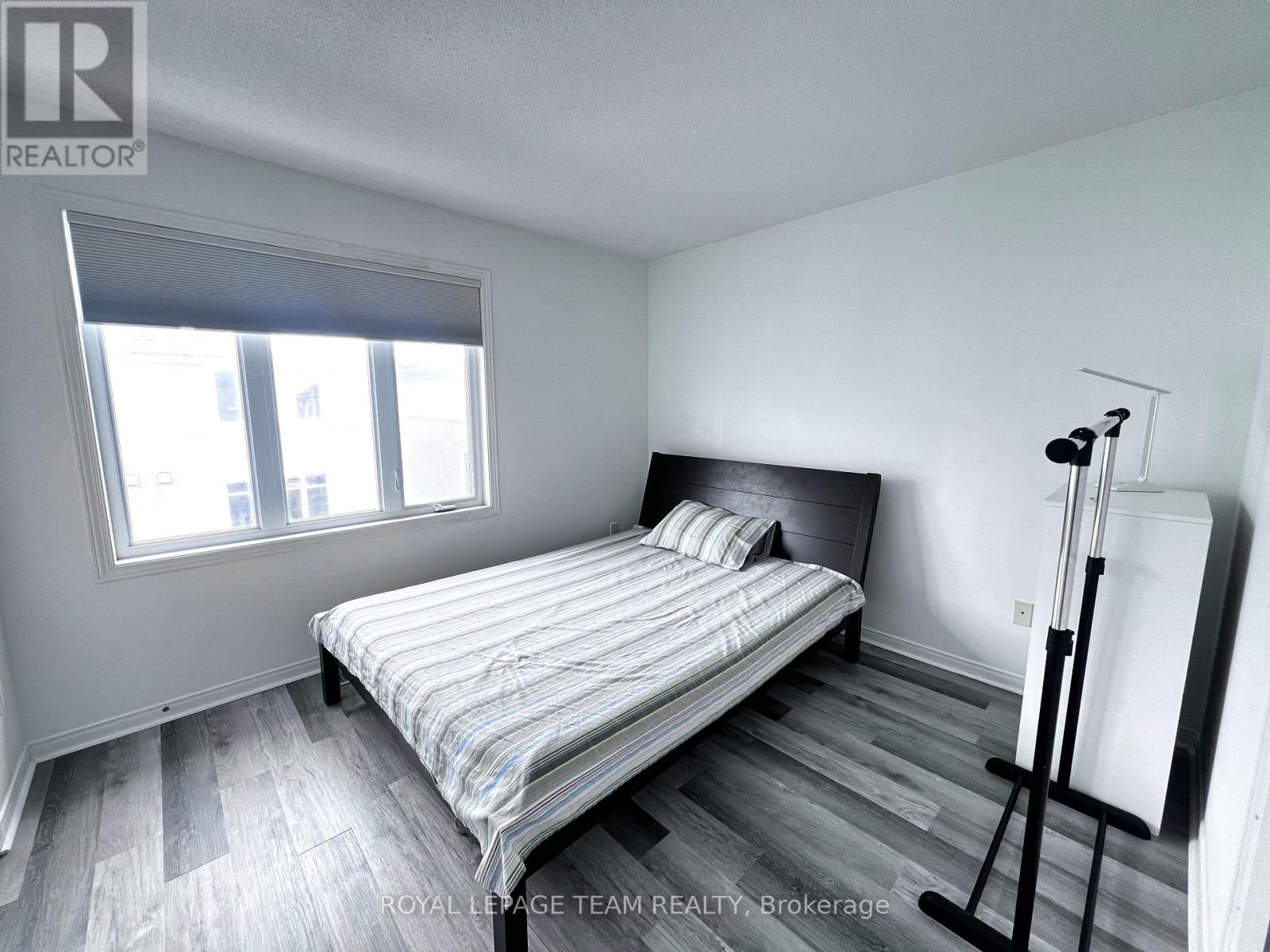 A bedroom with a bed, wooden floors, and a window.