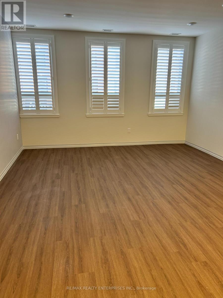 A room with wooden flooring and three windows.