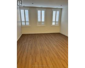 A room with wooden flooring and three windows.