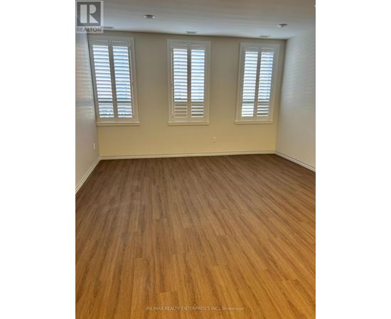 A room with wooden flooring and three windows.