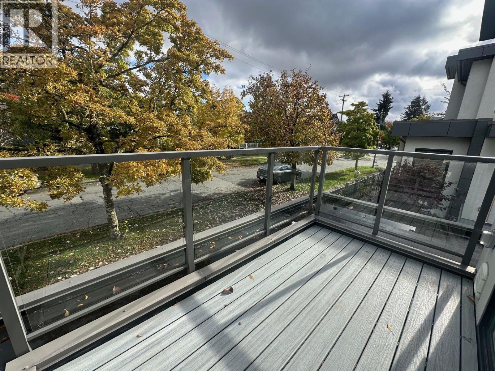 A wooden deck with a metal railing and a view of a street and trees.