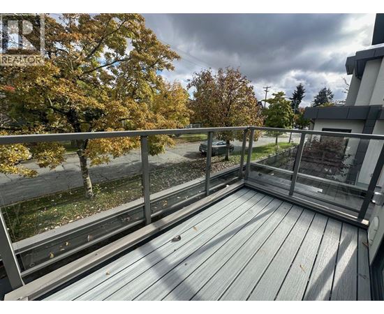 A wooden deck with a metal railing and a view of a street and trees.