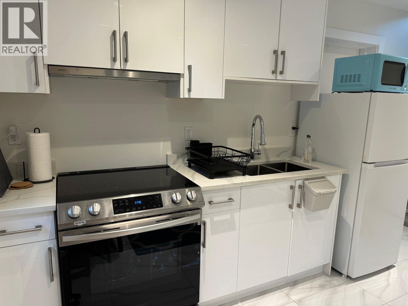 A modern kitchen with white cabinets and a black stove top oven.