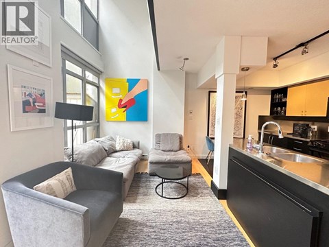 A living room with a grey couch and a grey armchair with a small round table between them.