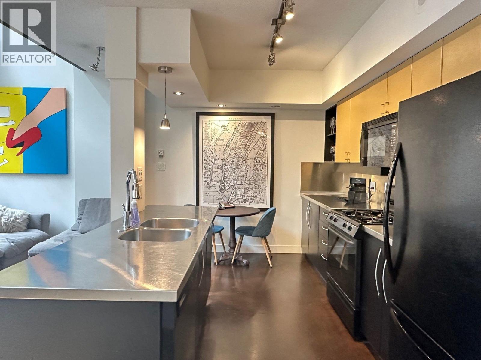 A modern kitchen with a black refrigerator and a painting on the wall.