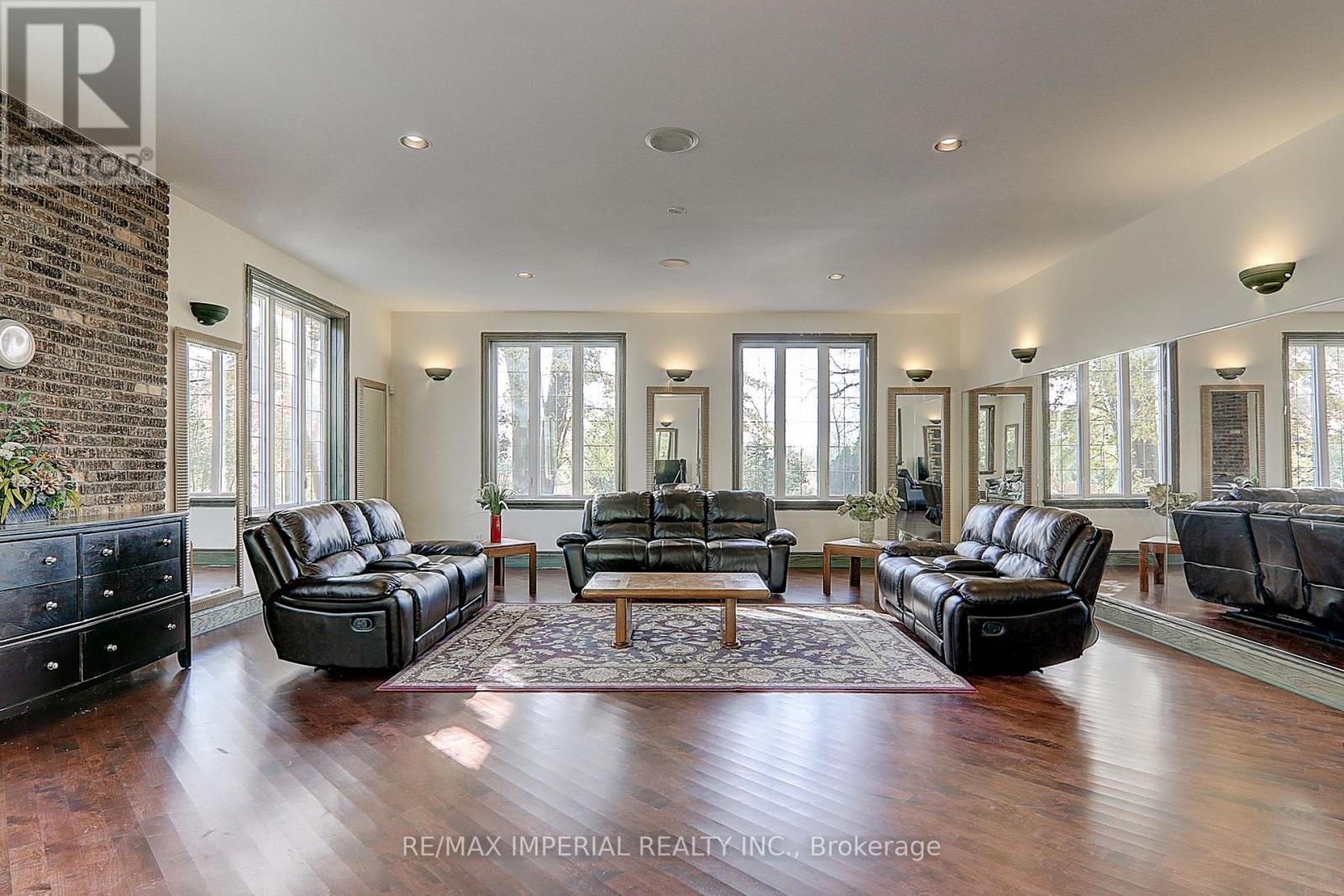 A spacious living room with black leather furniture and a brick accent wall.