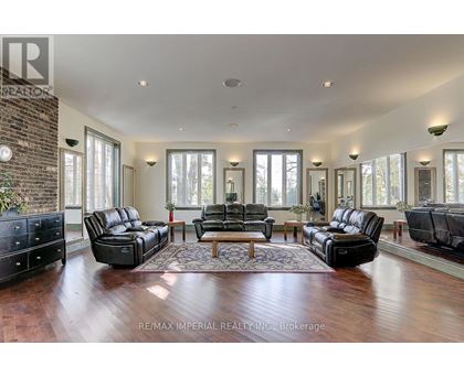 A spacious living room with black leather furniture and a brick accent wall.